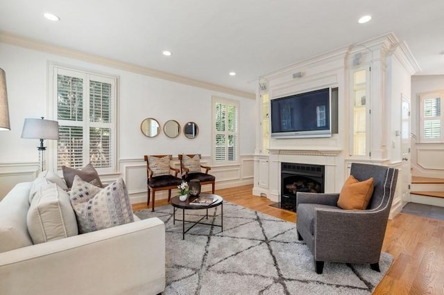 living area featuring a fireplace with flush hearth, wainscoting, crown molding, and light wood-type flooring