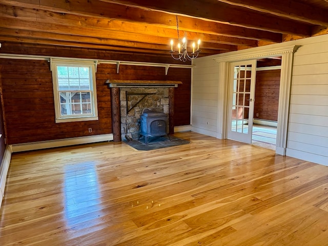 unfurnished living room with an inviting chandelier, wooden walls, a wood stove, baseboard heating, and beam ceiling