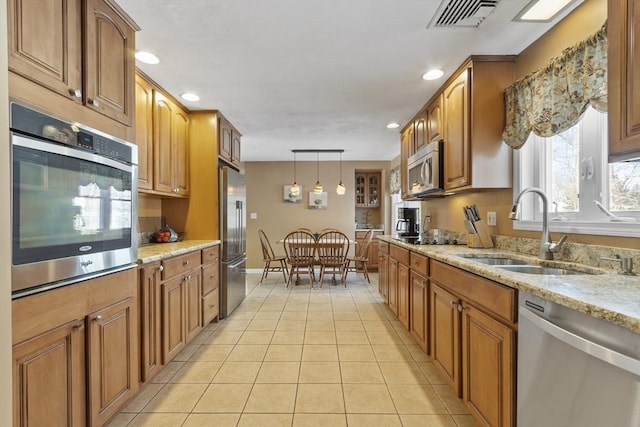 kitchen with sink, stainless steel appliances, hanging light fixtures, and light stone countertops