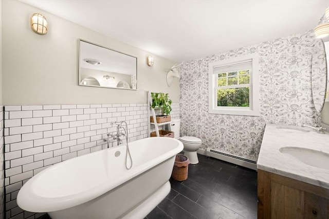 full bath with baseboard heating, wallpapered walls, a freestanding bath, toilet, and double vanity
