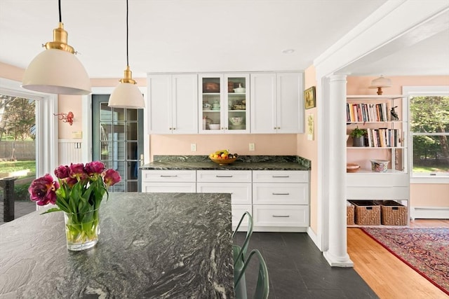 kitchen featuring white cabinetry, glass insert cabinets, dark stone countertops, and decorative columns