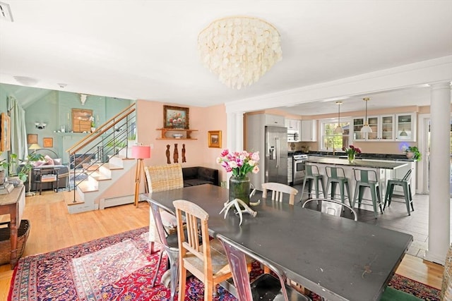 dining area with decorative columns, light wood finished floors, and stairway