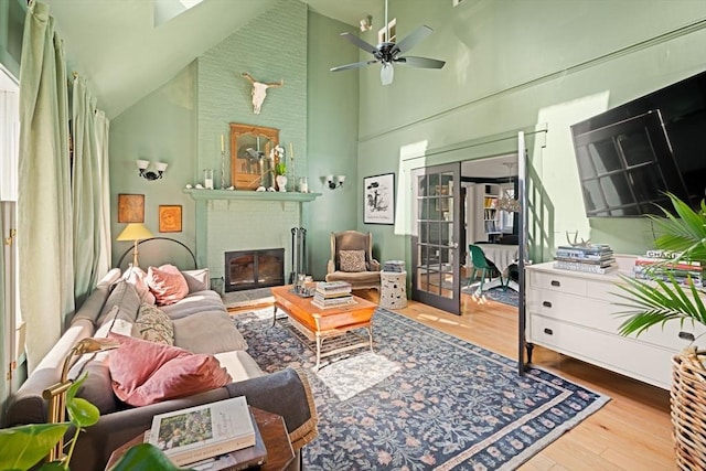 living area featuring high vaulted ceiling, wood finished floors, a brick fireplace, ceiling fan, and french doors