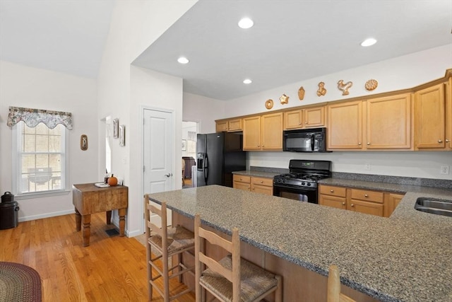 kitchen featuring sink, kitchen peninsula, a breakfast bar area, black appliances, and light wood-type flooring