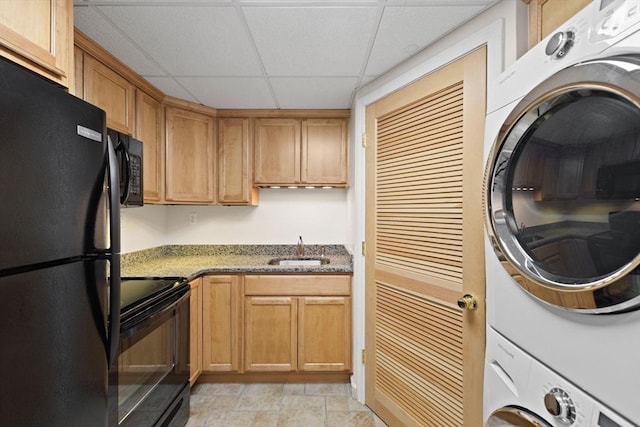 kitchen featuring a drop ceiling, sink, stacked washing maching and dryer, dark stone countertops, and black appliances