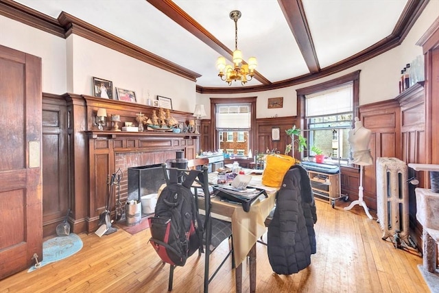 dining room featuring a chandelier, ornamental molding, a fireplace, light wood-style floors, and a wainscoted wall