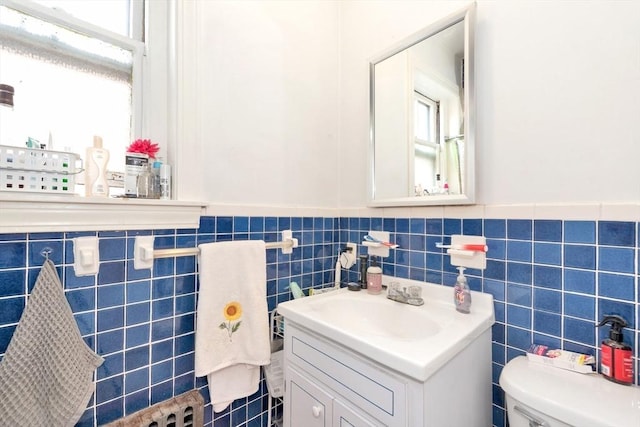 half bathroom featuring tile walls, a wainscoted wall, vanity, and toilet