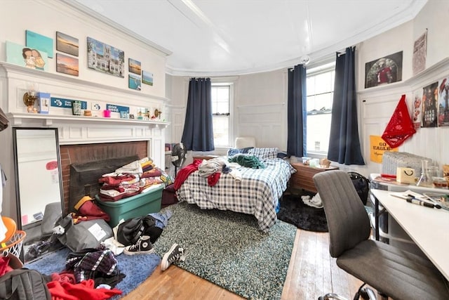 bedroom featuring wood finished floors, ornamental molding, a fireplace, and a decorative wall