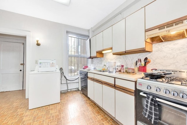 kitchen featuring stainless steel range with gas cooktop, washer / dryer, light countertops, under cabinet range hood, and decorative backsplash
