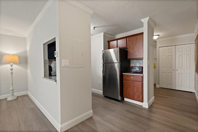 kitchen featuring hardwood / wood-style floors, decorative backsplash, crown molding, and stainless steel refrigerator