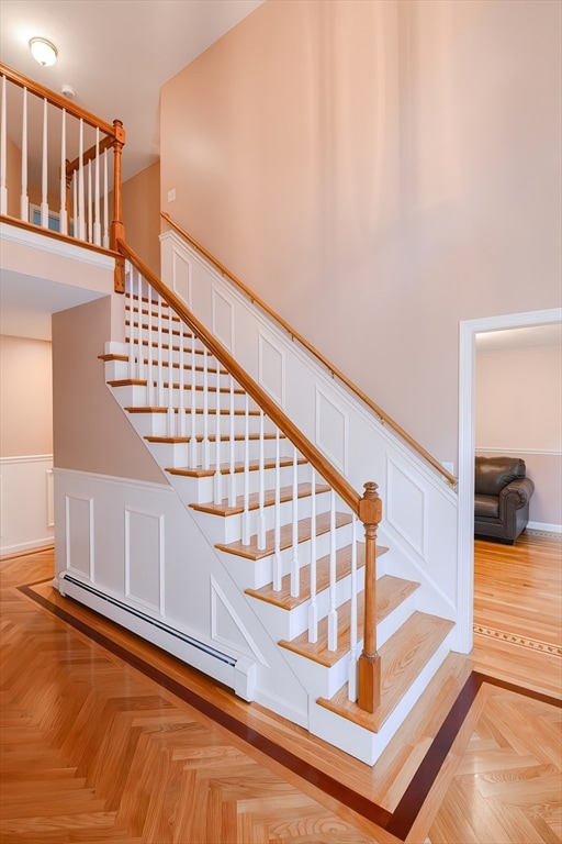 staircase with baseboard heating, a high ceiling, and parquet flooring