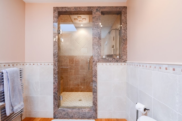 bathroom with hardwood / wood-style flooring, a shower with shower door, tile walls, and radiator