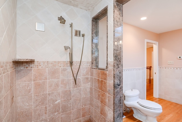 bathroom with hardwood / wood-style floors, toilet, a tile shower, and tile walls