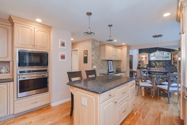 kitchen with stainless steel oven, pendant lighting, light hardwood / wood-style flooring, a center island, and a breakfast bar area