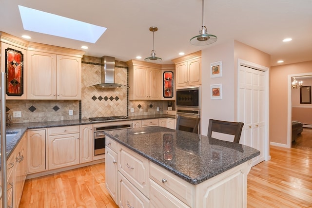 kitchen featuring hanging light fixtures, wall chimney range hood, tasteful backsplash, light hardwood / wood-style flooring, and a kitchen island