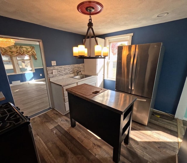 kitchen featuring sink, stainless steel fridge, a textured ceiling, decorative light fixtures, and dark hardwood / wood-style flooring