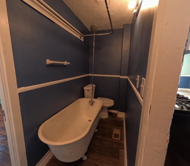 bathroom with a washtub, hardwood / wood-style floors, a textured ceiling, and toilet