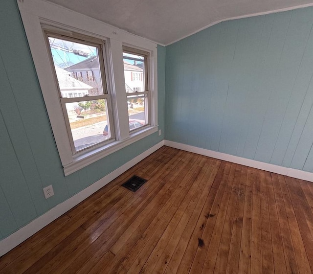 spare room featuring wood walls, hardwood / wood-style floors, and lofted ceiling