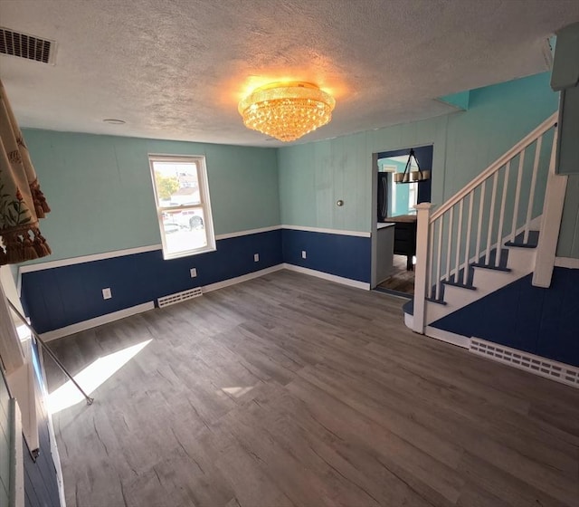 empty room featuring a chandelier, wood-type flooring, and a textured ceiling