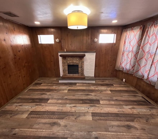 unfurnished living room featuring a stone fireplace, wooden walls, a healthy amount of sunlight, and hardwood / wood-style flooring