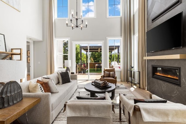 living room with an inviting chandelier, plenty of natural light, a large fireplace, and light wood-type flooring