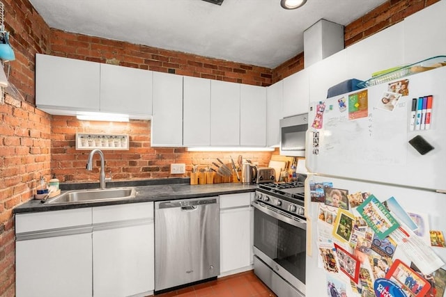 kitchen featuring appliances with stainless steel finishes, a sink, dark countertops, and white cabinetry