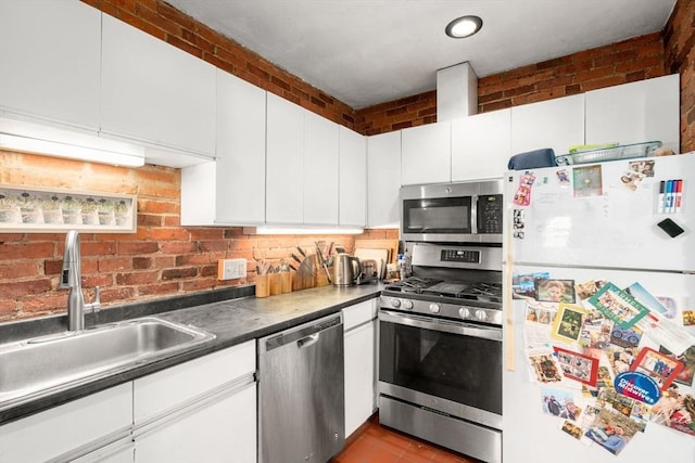 kitchen with appliances with stainless steel finishes, a sink, white cabinetry, dark countertops, and tile patterned flooring