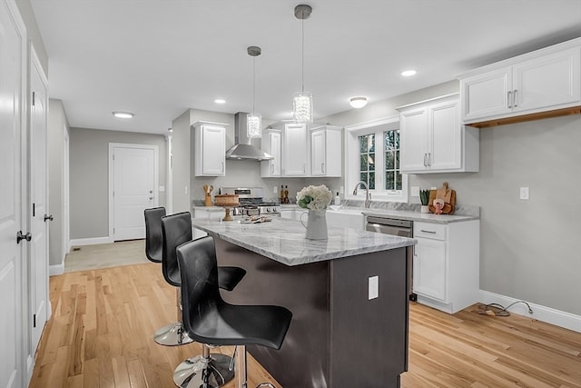 kitchen with white cabinetry, decorative light fixtures, wall chimney range hood, and appliances with stainless steel finishes