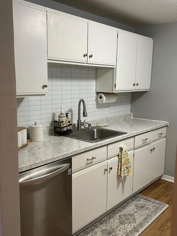 kitchen with sink, a textured ceiling, dark hardwood / wood-style flooring, dishwasher, and white cabinets