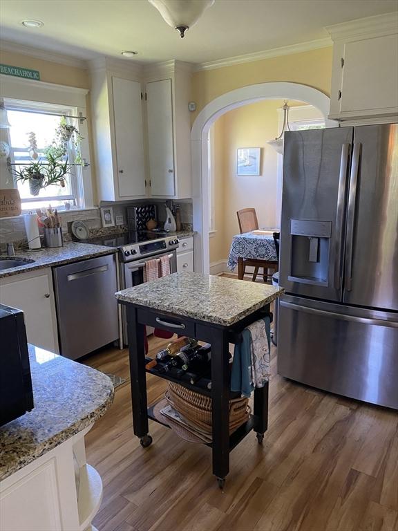 452 W Clinton St, New Bedford, MA 02740 - kitchen with stainless steel appliances, arched walkways, white cabinets, wood finished floors, and crown molding