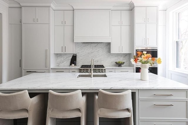 240 Commonwealth Ave Unit 2, Boston, MA 02116 - kitchen featuring a sink, backsplash, a kitchen bar, an island with sink, and light stone counters