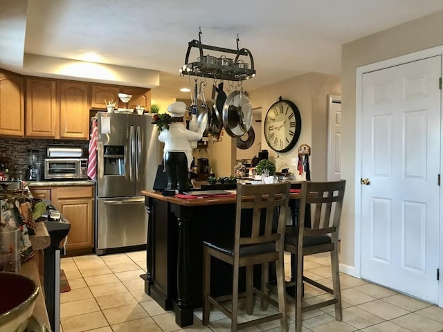 kitchen with tasteful backsplash, stainless steel fridge with ice dispenser, a breakfast bar area, and light tile patterned floors