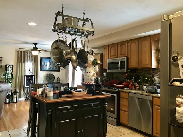 kitchen with light tile patterned floors, ceiling fan, appliances with stainless steel finishes, backsplash, and a center island