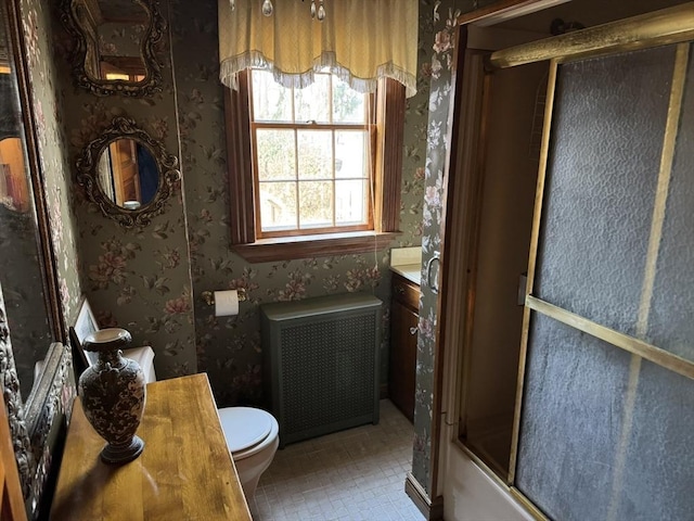 full bathroom featuring vanity, radiator heating unit, toilet, and bath / shower combo with glass door