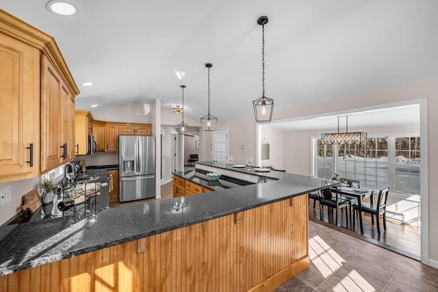 kitchen with decorative light fixtures, lofted ceiling, dark stone countertops, a peninsula, and stainless steel fridge with ice dispenser