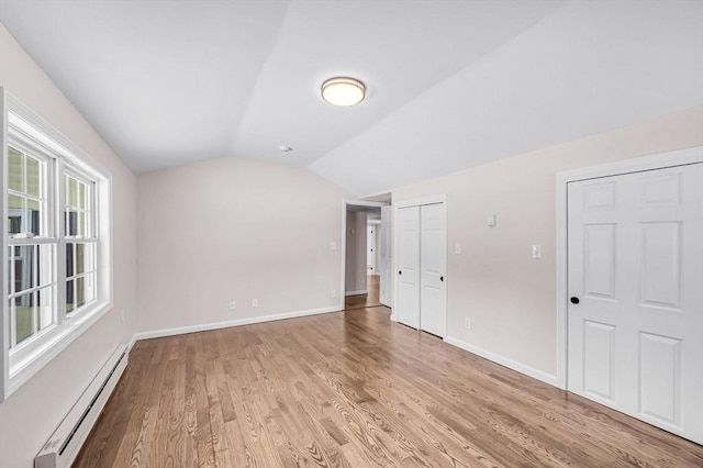 interior space with vaulted ceiling, baseboard heating, baseboards, and light wood-style floors