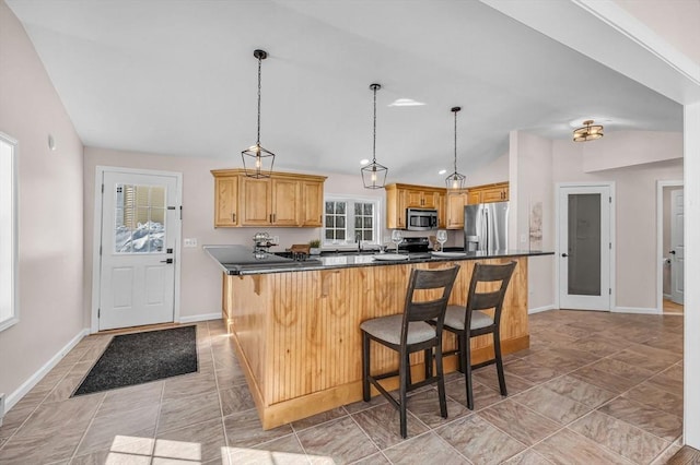 kitchen with baseboards, dark countertops, appliances with stainless steel finishes, a kitchen breakfast bar, and vaulted ceiling