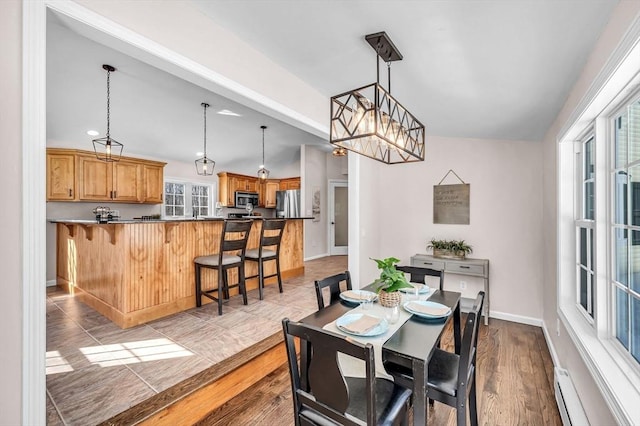 dining room featuring a baseboard heating unit, lofted ceiling, light wood finished floors, and baseboards