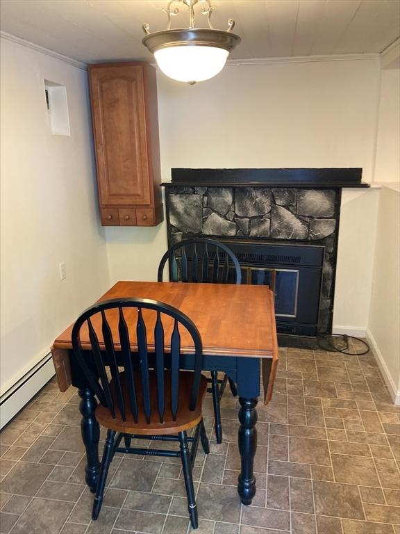 dining area featuring crown molding, baseboards, baseboard heating, and a stone fireplace