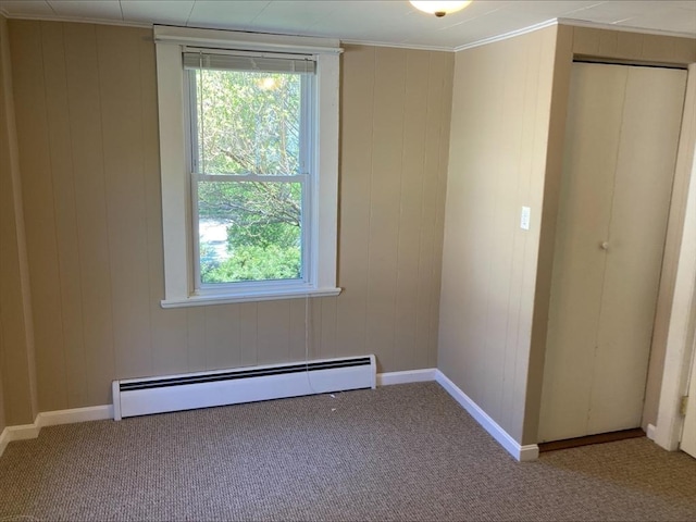 carpeted empty room featuring plenty of natural light, a baseboard radiator, baseboards, and wood walls