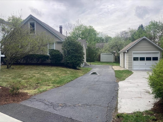 view of side of property featuring a garage, aphalt driveway, a chimney, an outbuilding, and a yard