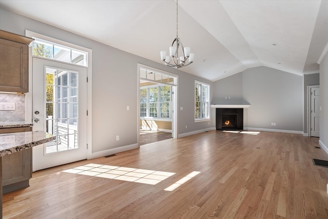 unfurnished living room featuring lofted ceiling, a chandelier, and light hardwood / wood-style flooring