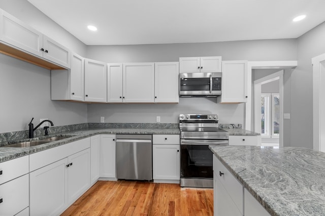 kitchen with sink, stainless steel appliances, light stone counters, light hardwood / wood-style flooring, and white cabinets