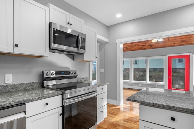 kitchen with white cabinets, light hardwood / wood-style floors, dark stone countertops, and stainless steel appliances