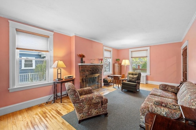 living area with baseboards, a fireplace with flush hearth, ornamental molding, and hardwood / wood-style floors