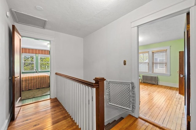 hall with radiator, attic access, hardwood / wood-style flooring, and visible vents