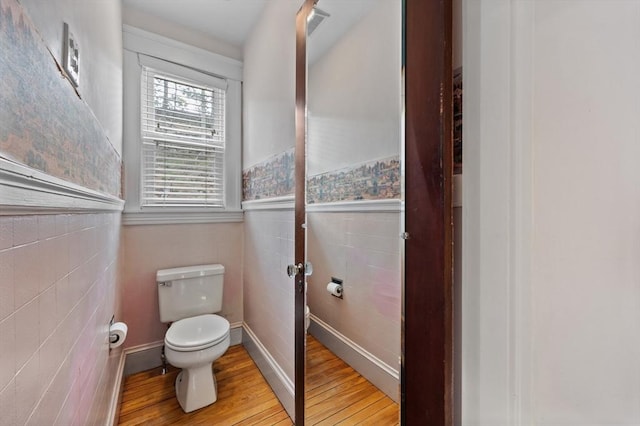 bathroom featuring wainscoting, wood finished floors, toilet, and tile walls