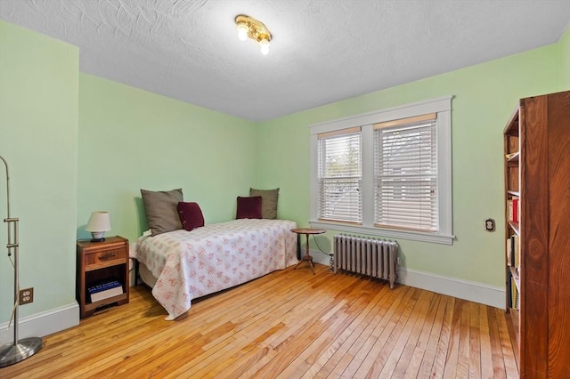 bedroom featuring baseboards, light wood-style flooring, and radiator heating unit