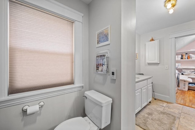 half bathroom with toilet, baseboards, stone finish floor, and vanity