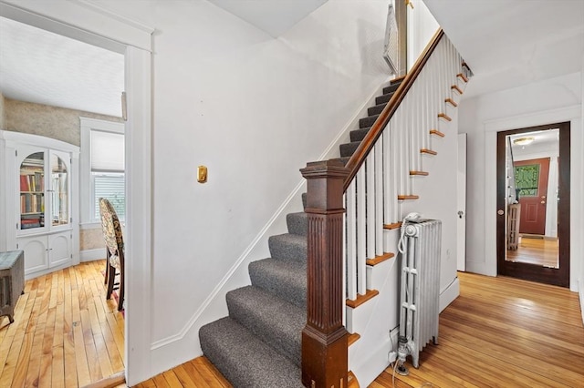 stairway featuring baseboards, plenty of natural light, radiator, and hardwood / wood-style floors